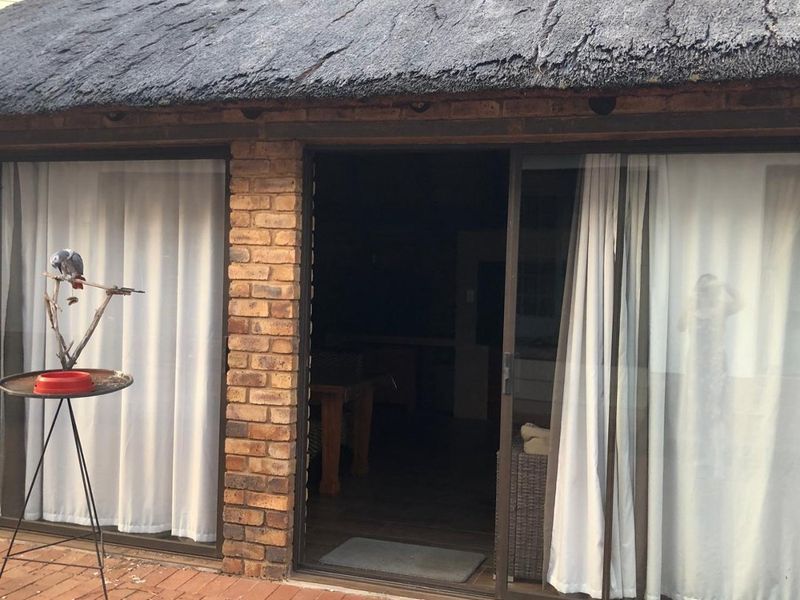A covered patio area featuring brick paving, sliding glass doors, and a traditional thatch roof structure.