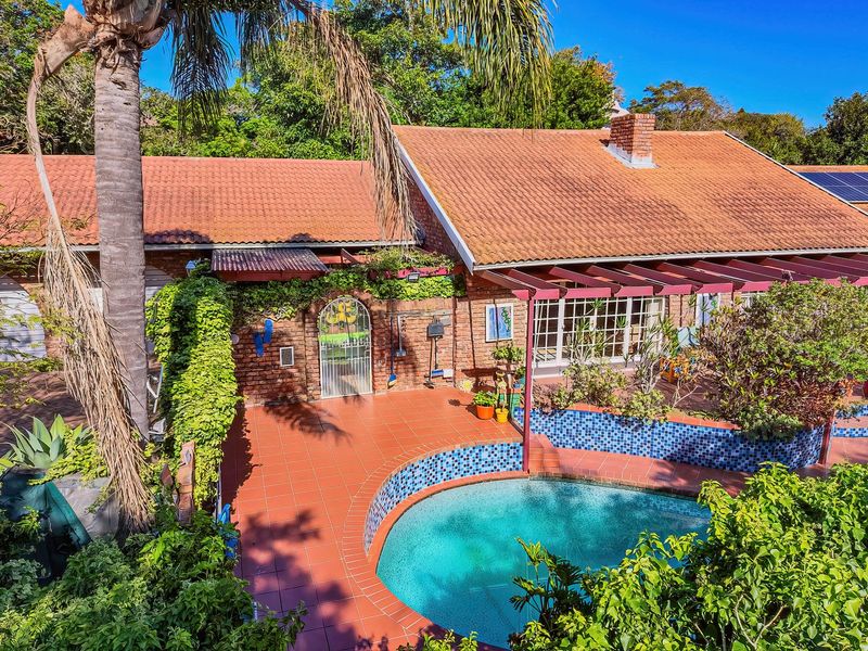 Rear exterior view featuring a swimming pool with tiled surround, a covered patio area, and a classic brick house with terracotta roof tiles.