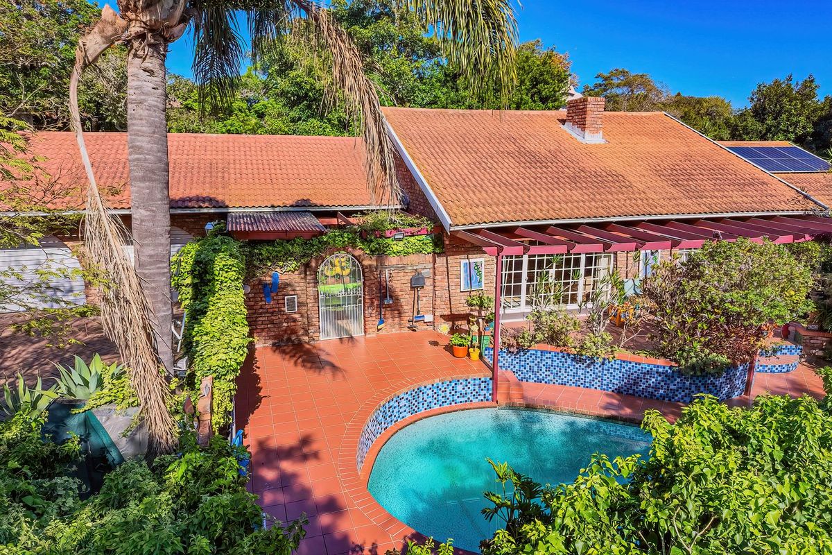 Rear exterior view featuring a swimming pool with tiled surround, a covered patio area, and a classic brick house with terracotta roof tiles.