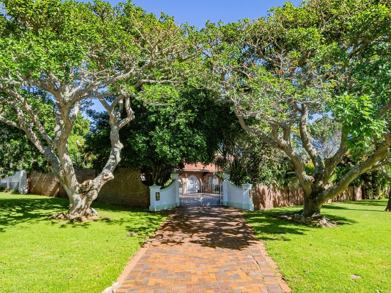 A well-maintained front entrance featuring a brick paved driveway, gated access, and mature trees set within a lush, landscaped garden.