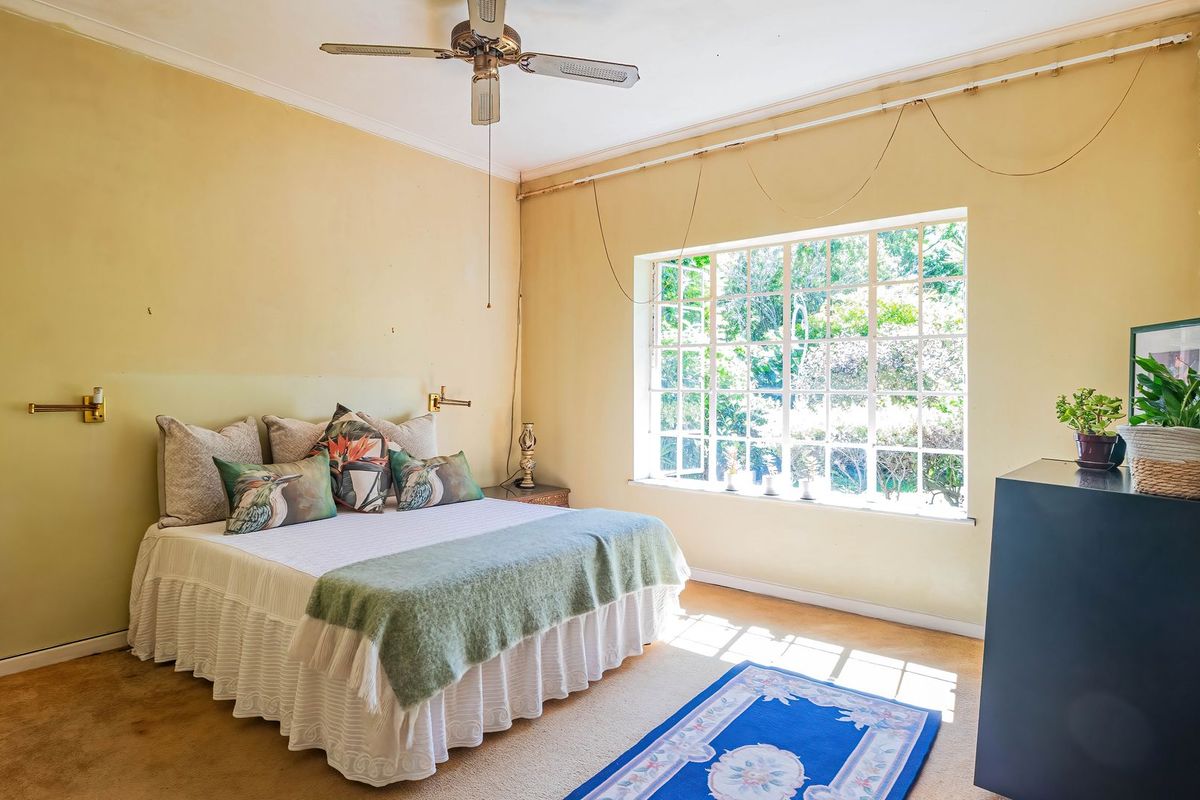 A bedroom featuring a large multi-pane window, built-in cupboards, and a ceiling fan, requiring cosmetic updates to the flooring and wall finishes.
