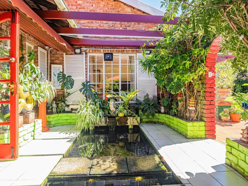A charming covered patio area featuring a built-in water feature, brick wall construction, and direct access to the home through a vibrant red door.