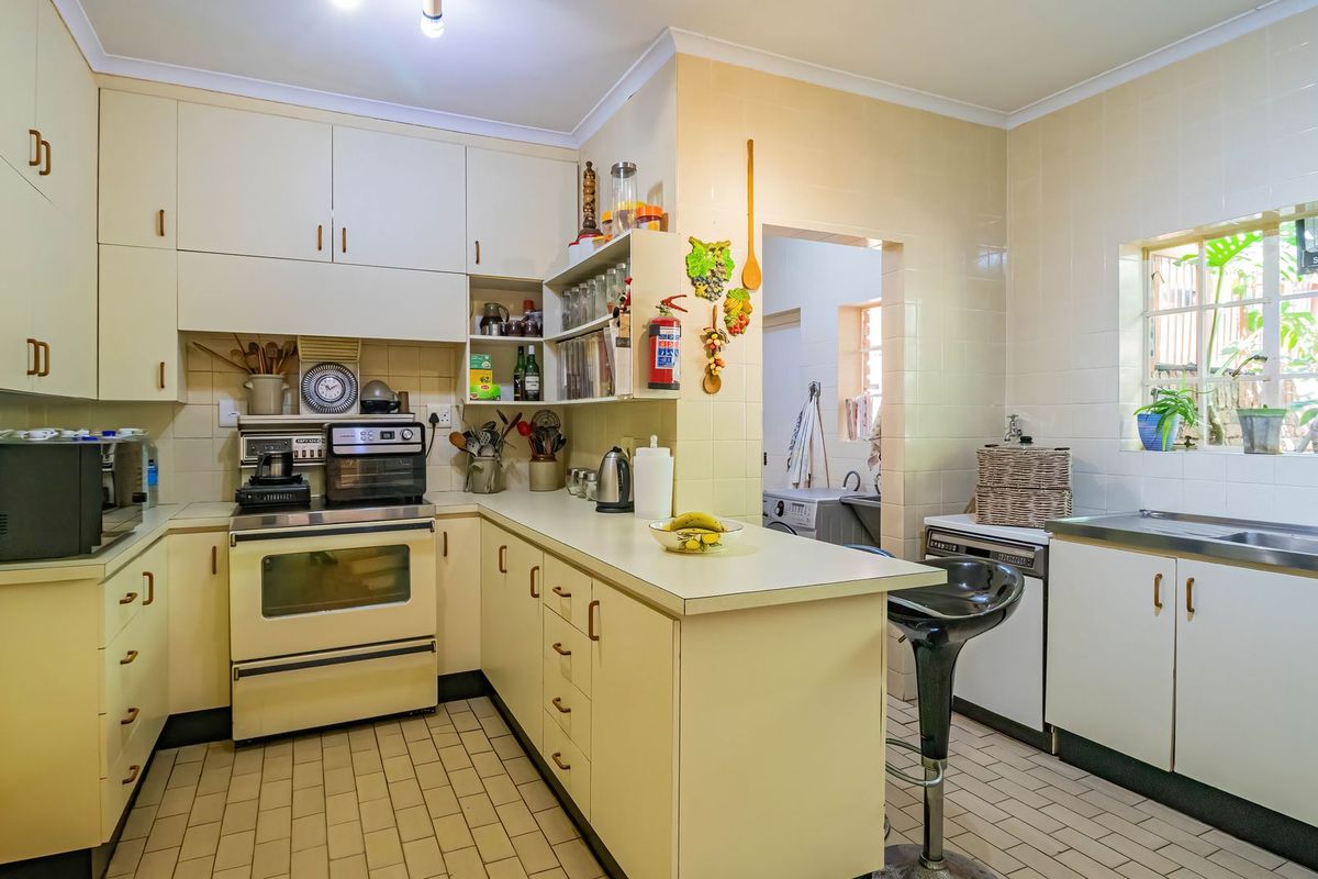 A functional kitchen featuring built-in cabinetry, laminate countertops, a built-in oven, and tiled finishes, with an adjacent scullery area visible.