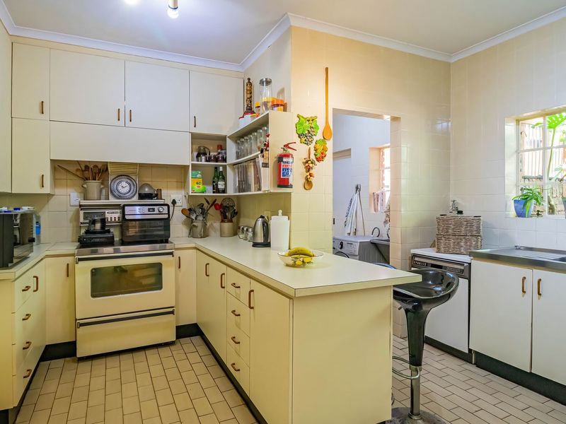 A functional kitchen featuring built-in cabinetry, laminate countertops, a built-in oven, and tiled finishes, with an adjacent scullery area visible.