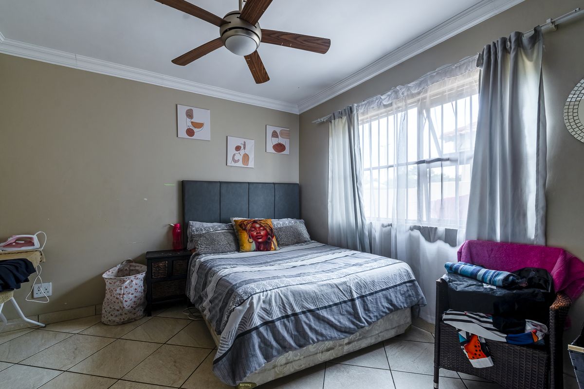 A bedroom featuring tiled flooring, a ceiling fan, and security bars on the window, providing a functional space with neutral wall tones.