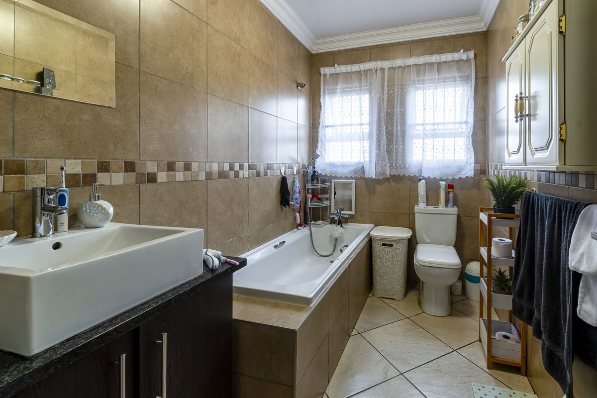 A functional bathroom featuring a built-in vanity, tiled walls and flooring, a bathtub with shower mixer, and a toilet.