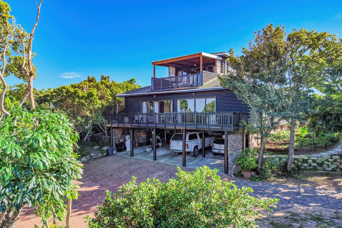 A multi-level residential property featuring dark corrugated metal cladding, expansive timber decking, and a stone-finished ground level with covered parking.