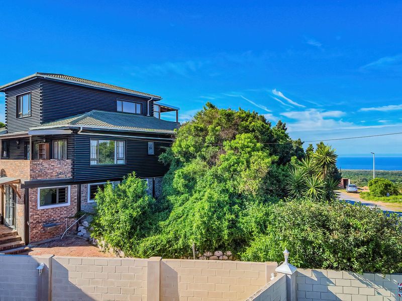 A multi-level residential property featuring a combination of brick and dark metal cladding, set within a landscaped garden with distant ocean views.