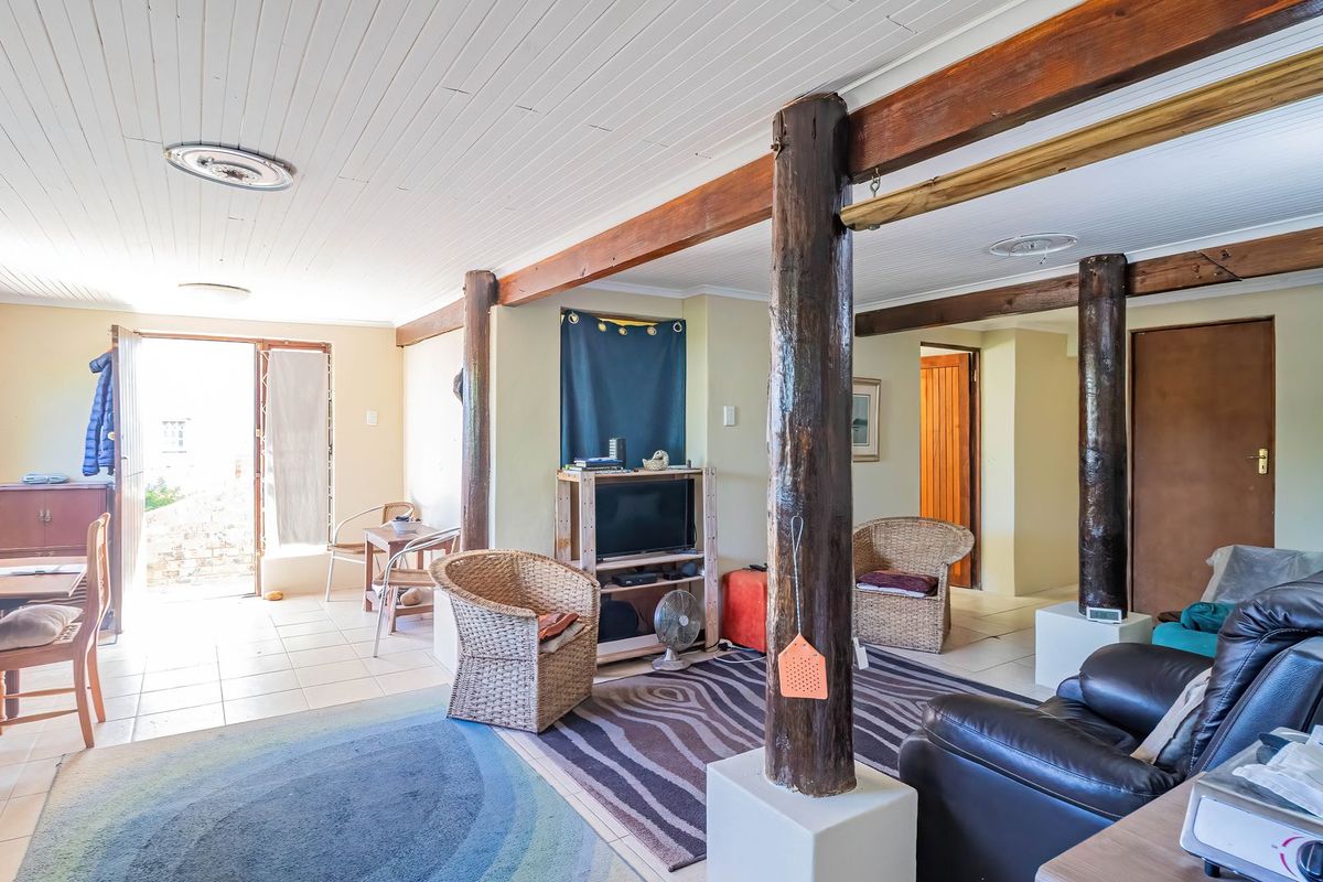 Spacious living area featuring exposed timber support beams, tiled flooring, and a timber ceiling with direct access to the outdoor area.