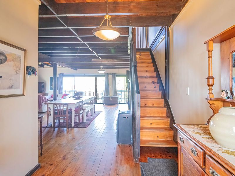 Open plan living and dining area featuring exposed timber ceiling beams, polished timber flooring, and a central timber staircase leading to the upper level.