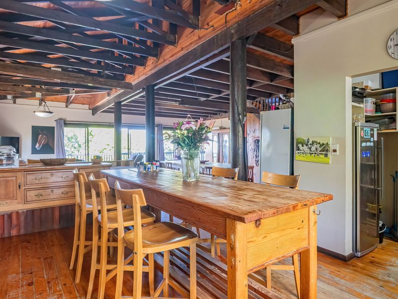 Spacious open-plan living and kitchen area featuring exposed timber ceiling beams, warm timber flooring, and a convenient built-in pantry storage unit.