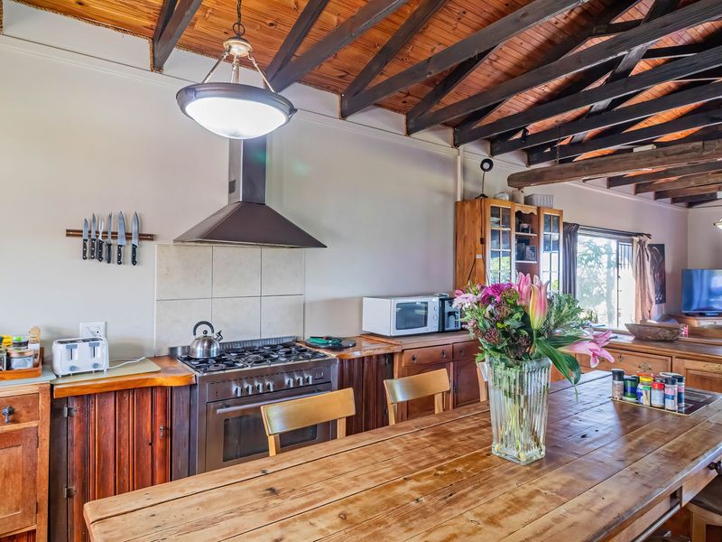 Open plan kitchen and dining area featuring exposed timber beam ceilings, rustic timber cabinetry, and a stainless steel gas stove with extractor fan.
