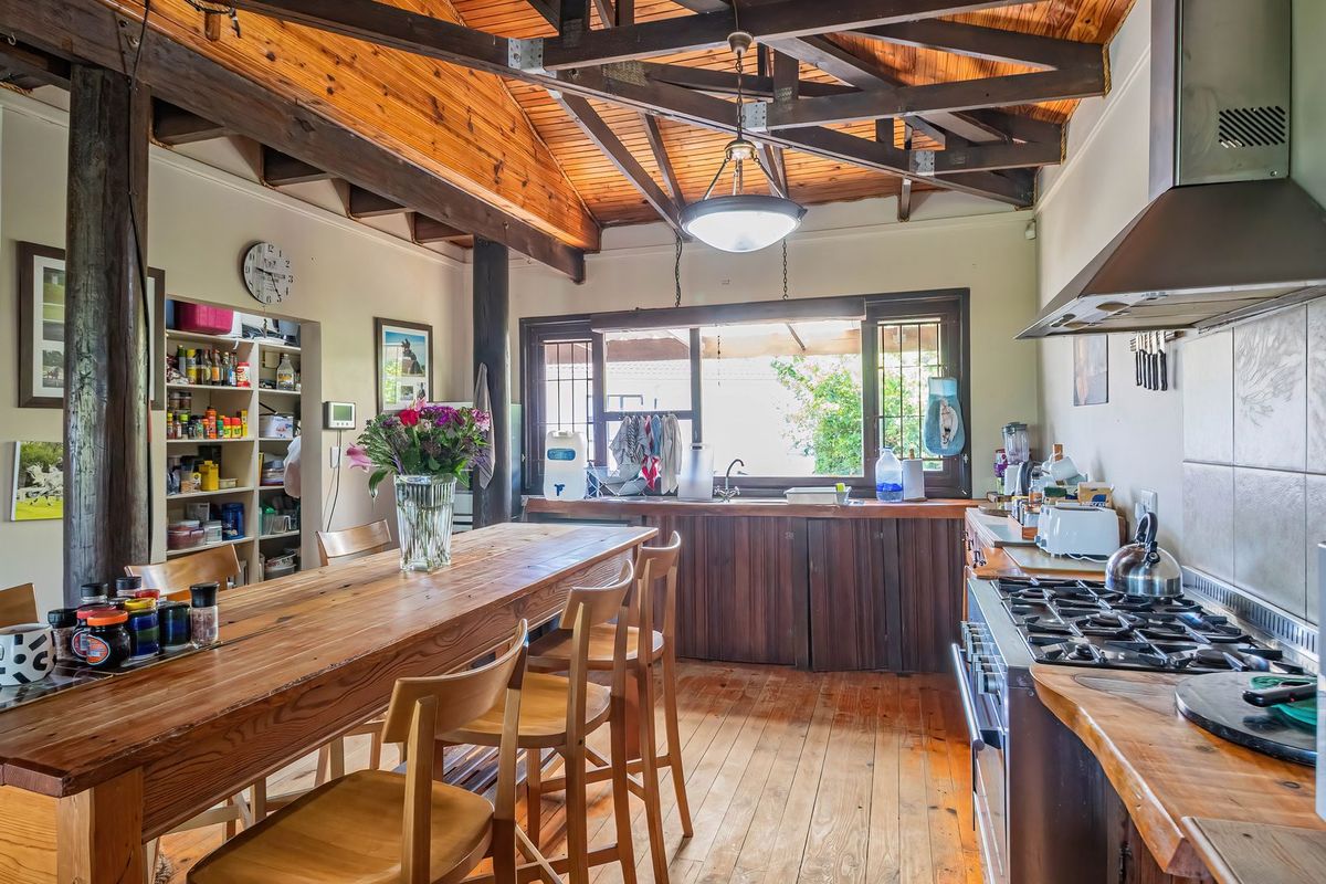 Rustic kitchen featuring exposed timber ceiling beams, wooden flooring, gas hob with extractor, and integrated pantry shelving, offering a warm, character-filled cooking space.