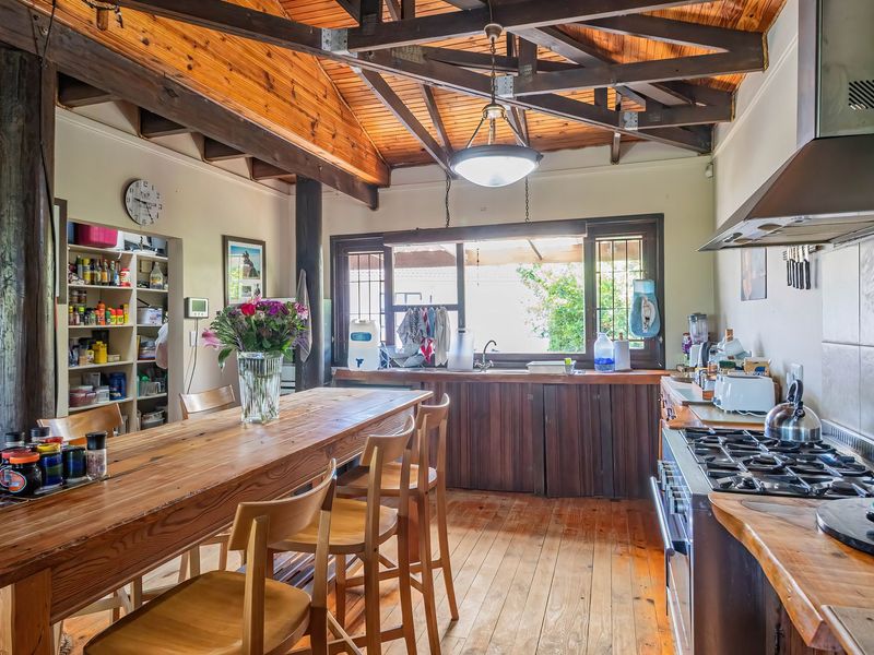 Rustic kitchen featuring exposed timber ceiling beams, wooden flooring, gas hob with extractor, and integrated pantry shelving, offering a warm, character-filled cooking space.