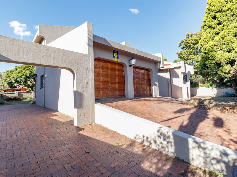 Front exterior view of the property featuring a double garage with wooden doors and a brick-paved driveway.