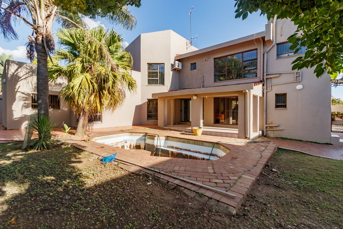 Rear view of the property featuring a covered patio and an empty swimming pool with brick paving in a garden setting.