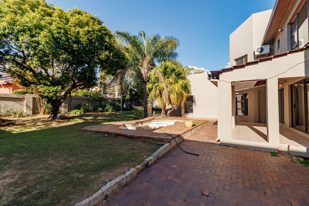 Rear exterior view featuring a paved patio, covered veranda, and a swimming pool set within a garden area with boundary walls.