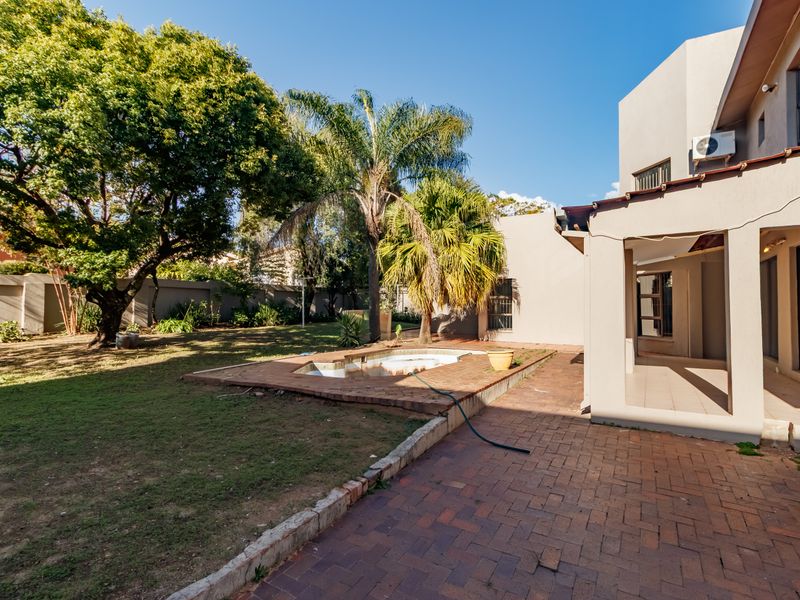 Rear exterior view featuring a paved patio, covered veranda, and a swimming pool set within a garden area with boundary walls.