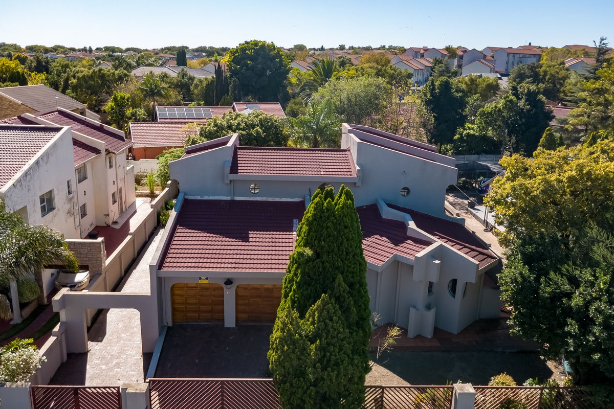 Aerial view of a residential property featuring a double garage, tiled roof, and paved driveway within a suburban neighborhood setting.