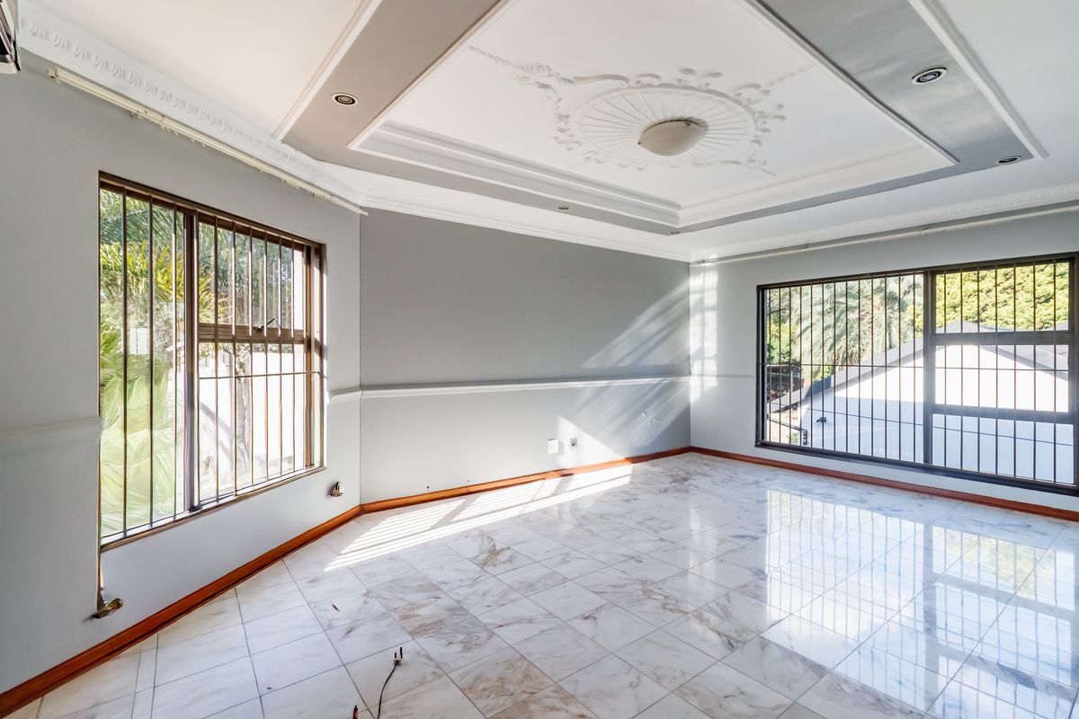 Spacious, light-filled living area featuring elegant crown molding, a decorative ceiling rose, recessed lighting, and polished marble-look floor tiles.