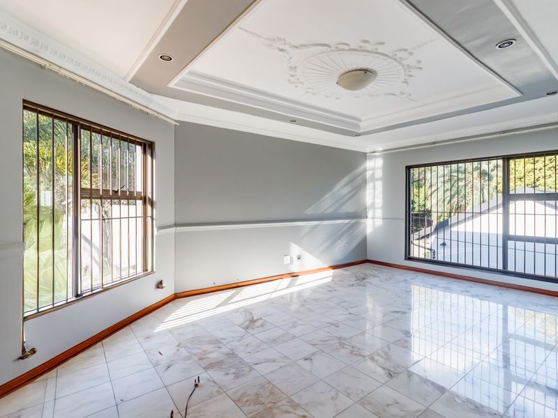 Spacious, light-filled living area featuring elegant crown molding, a decorative ceiling rose, recessed lighting, and polished marble-look floor tiles.