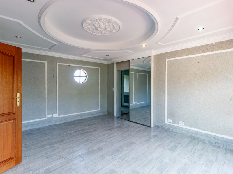 Spacious bedroom featuring decorative ceiling moulding, recessed lighting, a circular window, and built-in mirrored wardrobes with modern tiled flooring.