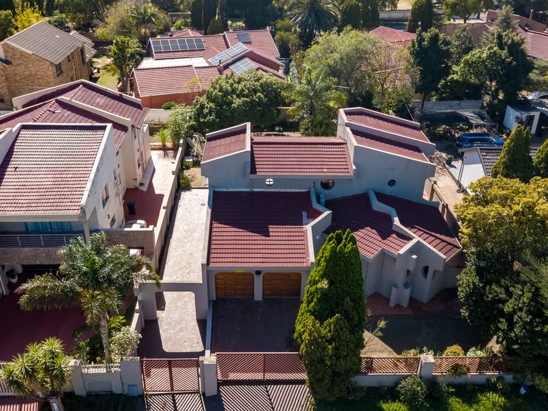 Aerial view of a residential property featuring a multi-level tiled roof, double garage, paved driveway, and secure perimeter fencing within a suburban neighborhood.