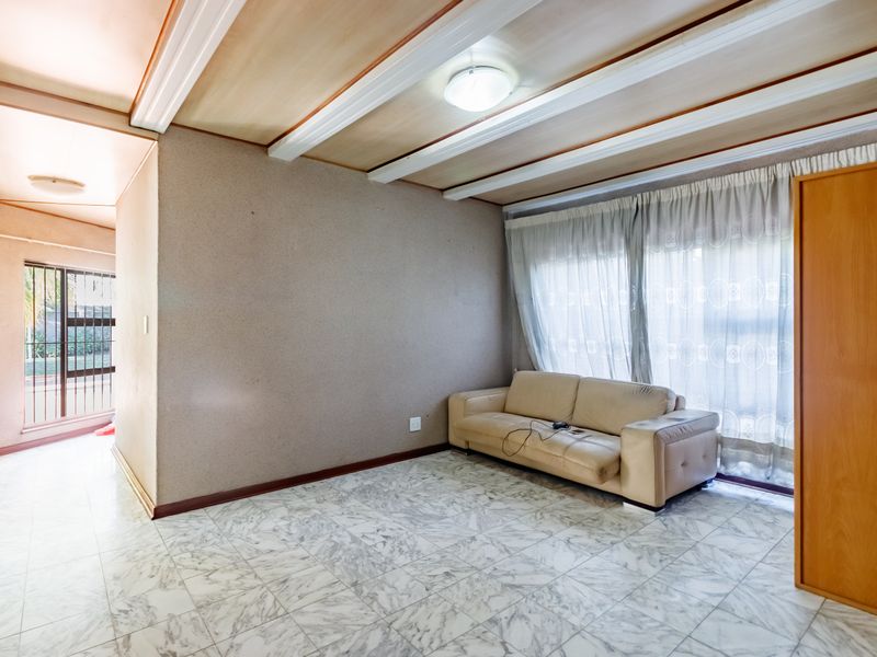 Living room featuring marble-look tile flooring, exposed beam ceiling, and a built-in cupboard, with access to an adjacent hallway area.
