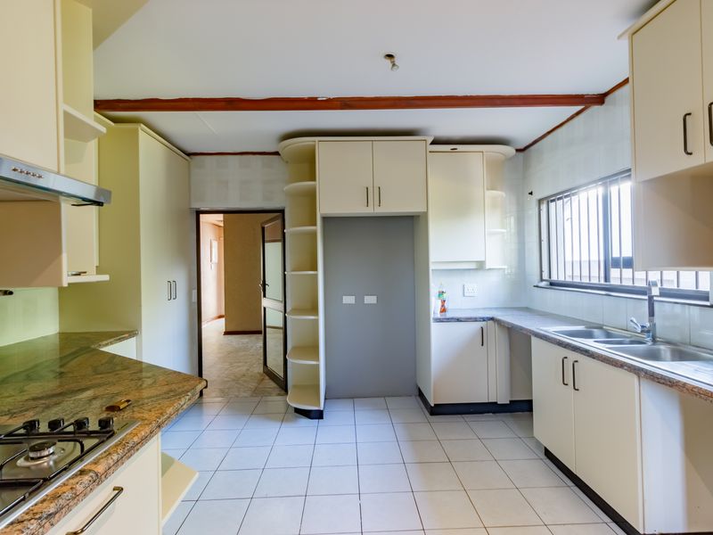 A functional kitchen featuring granite countertops, built-in cabinetry, a gas hob with extractor, and tiled flooring, offering a clean space ready for updates.