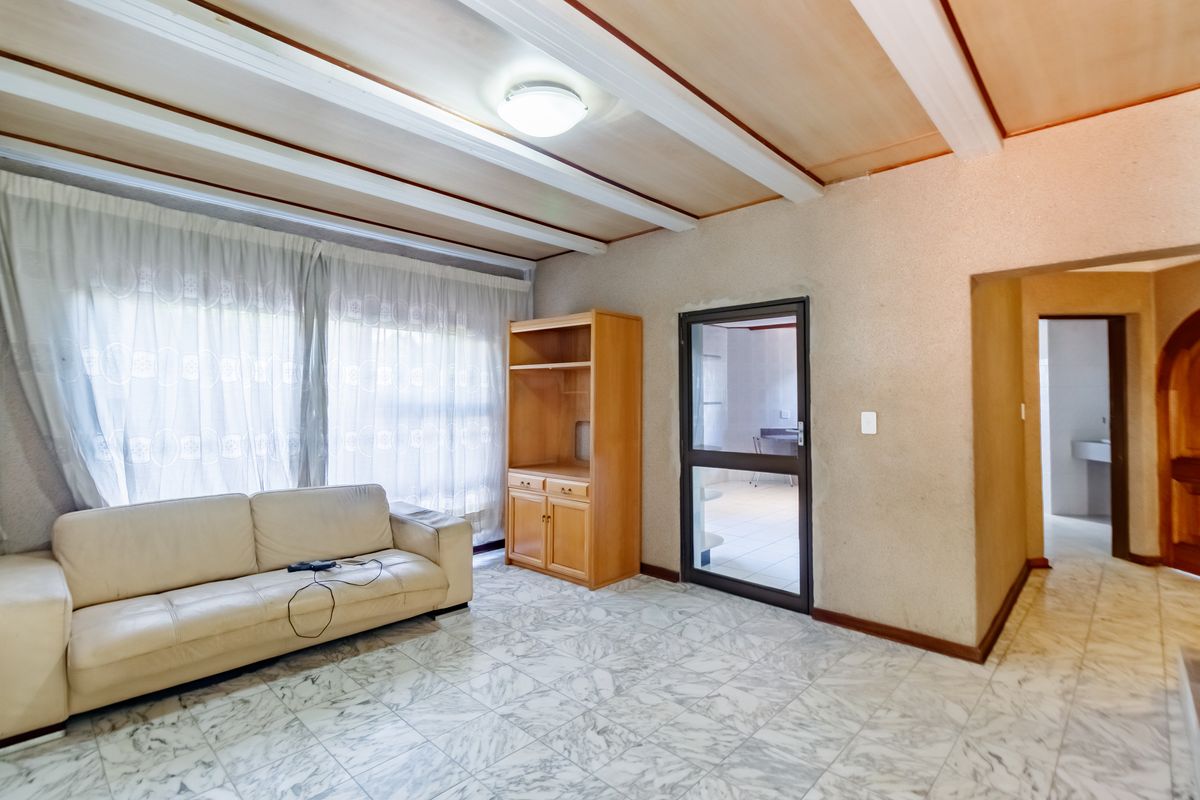 Living room featuring marble-look tiled flooring, exposed beam ceiling, and built-in cabinetry, with access to adjacent rooms through a glass-panelled door and archway.