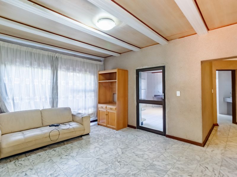 Living room featuring marble-look tiled flooring, exposed beam ceiling, and built-in cabinetry, with access to adjacent rooms through a glass-panelled door and archway.
