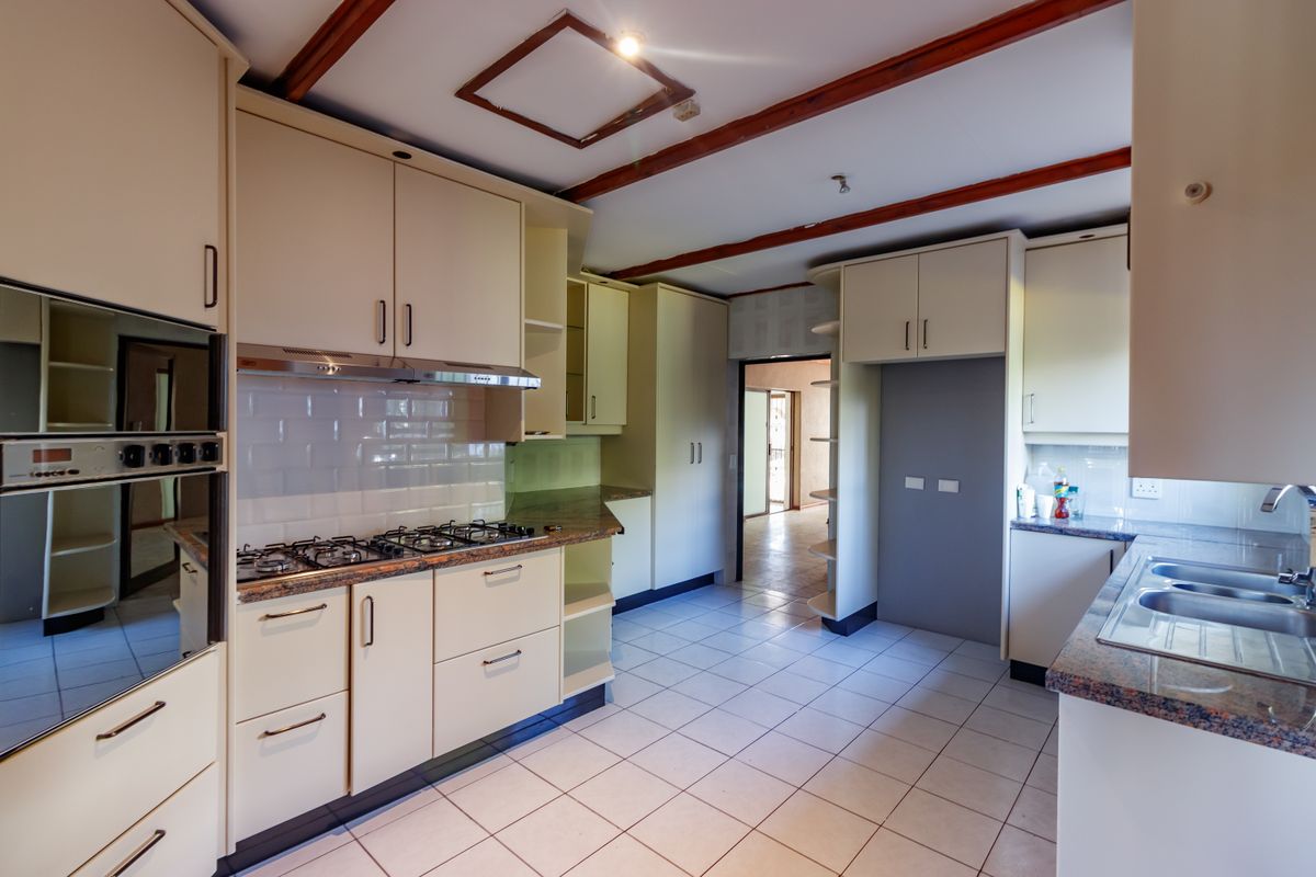 A functional kitchen featuring built-in oven, gas hob, granite countertops, and ample cabinetry, finished with tiled flooring and a subway tile backsplash.