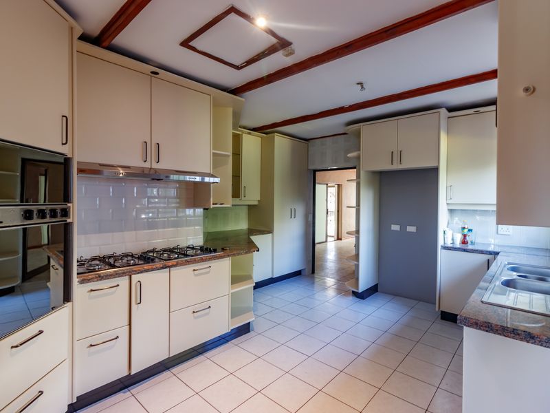 A functional kitchen featuring built-in oven, gas hob, granite countertops, and ample cabinetry, finished with tiled flooring and a subway tile backsplash.