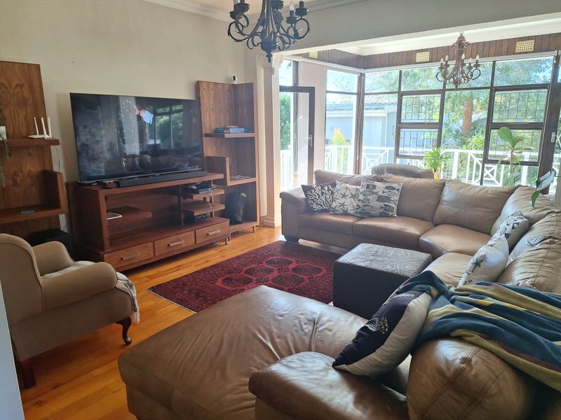 Spacious living room featuring hardwood flooring, large windows with natural light, and a built-in wooden shelving unit.