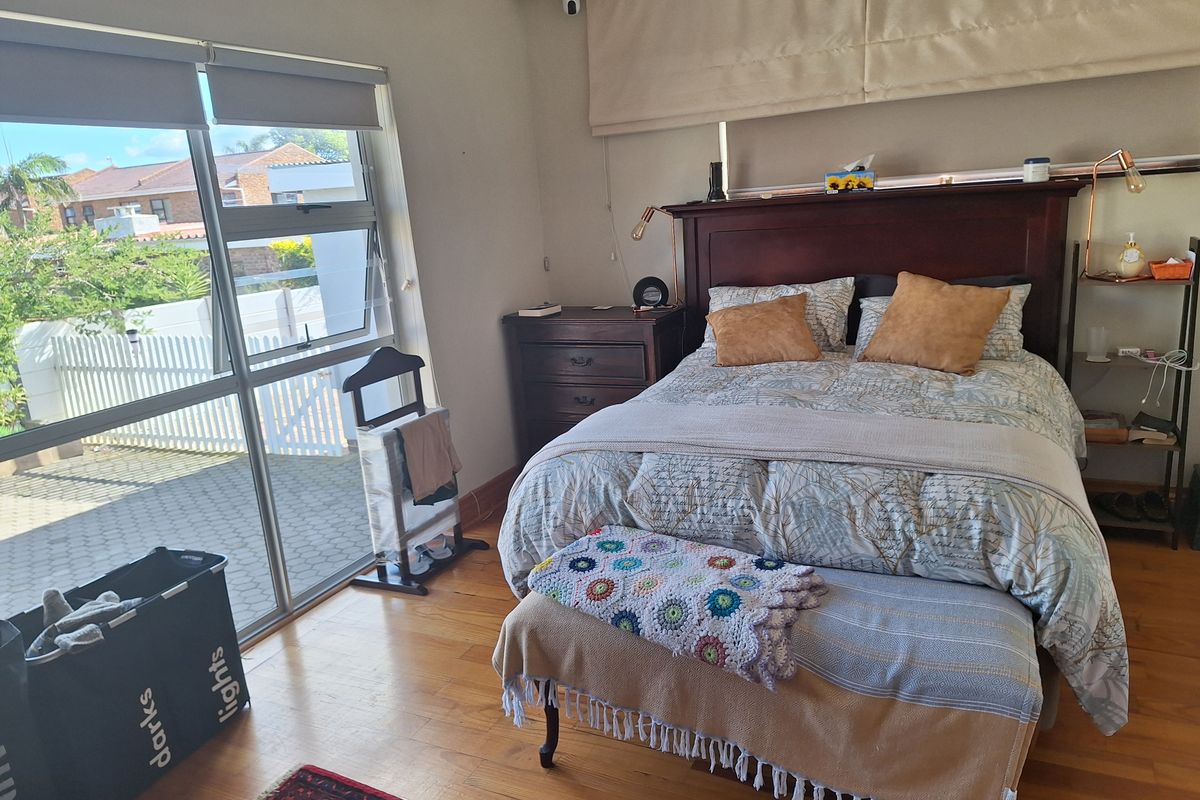 A well-maintained bedroom featuring timber flooring, a split-system air conditioner, and large sliding glass doors providing natural light and access to the exterior.