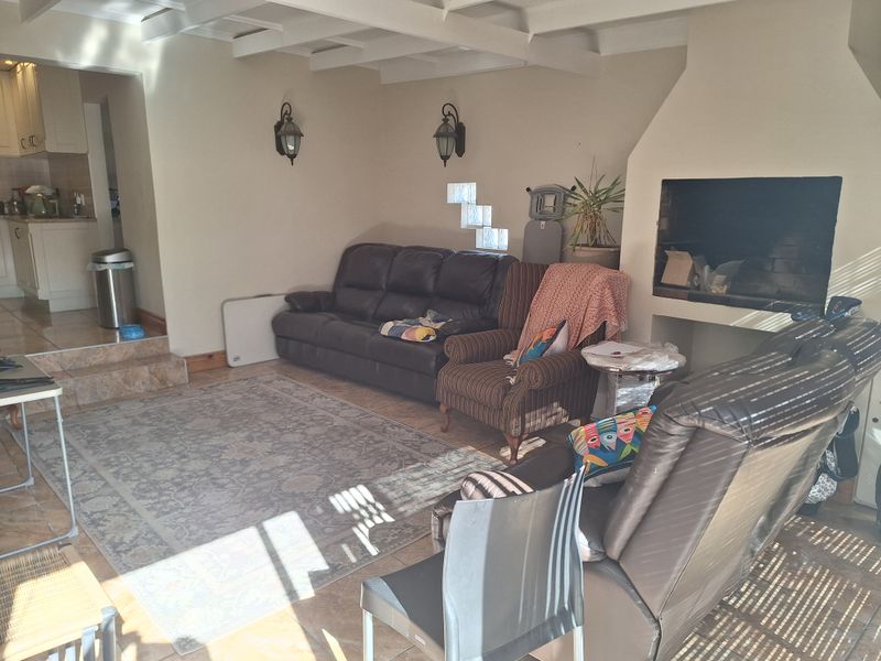A living room featuring exposed ceiling beams, a built-in fireplace, and a unique glass block window detail, with tiled flooring throughout.