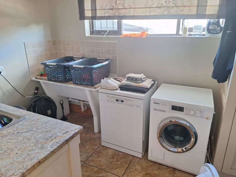 Functional laundry area featuring a built-in sink, granite countertops, tiled splashback, and dedicated space for laundry appliances.