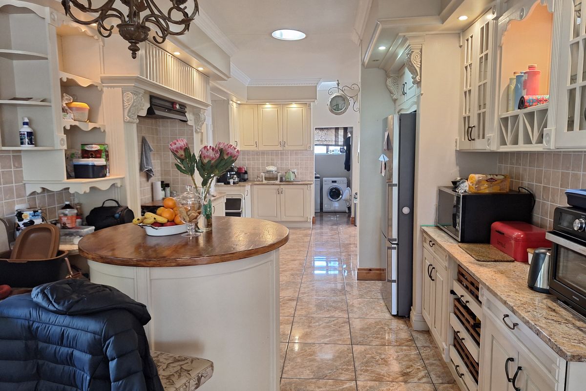 Spacious kitchen featuring classic cabinetry, granite countertops, a central island, and tiled flooring, with an adjacent laundry area visible in the background.