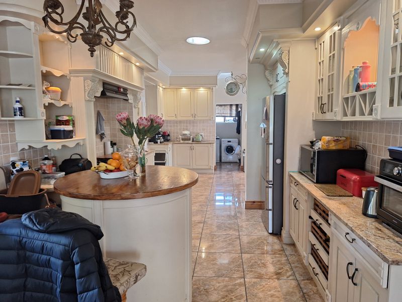 Spacious kitchen featuring classic cabinetry, granite countertops, a central island, and tiled flooring, with an adjacent laundry area visible in the background.