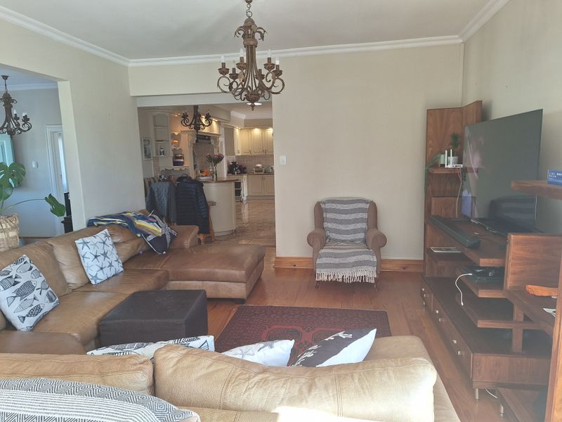 Open plan living area featuring hardwood flooring, crown molding, and a chandelier, with a view through to the kitchen area.