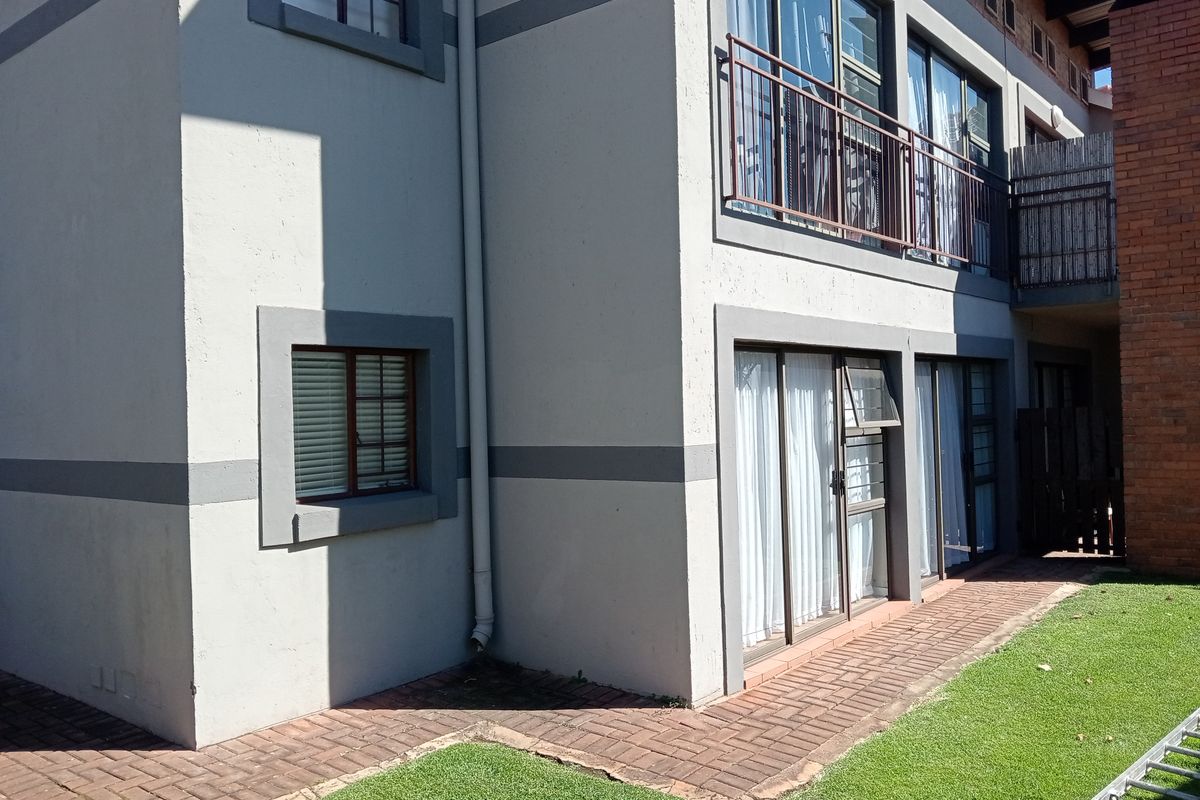 Rear view of the townhouse featuring a paved patio area, sliding glass doors, and a balcony with metal railings.