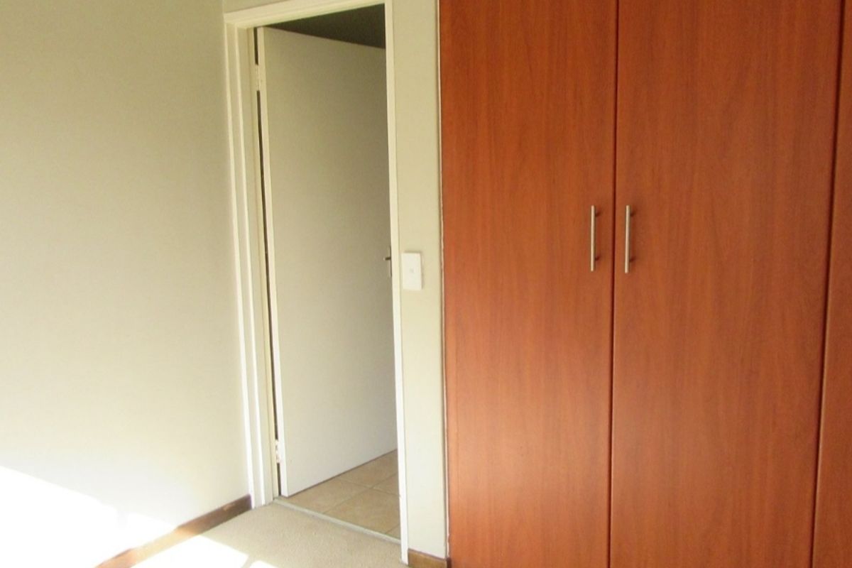 A clean, empty bedroom featuring neutral walls, carpeted flooring, and a large built-in wooden wardrobe.