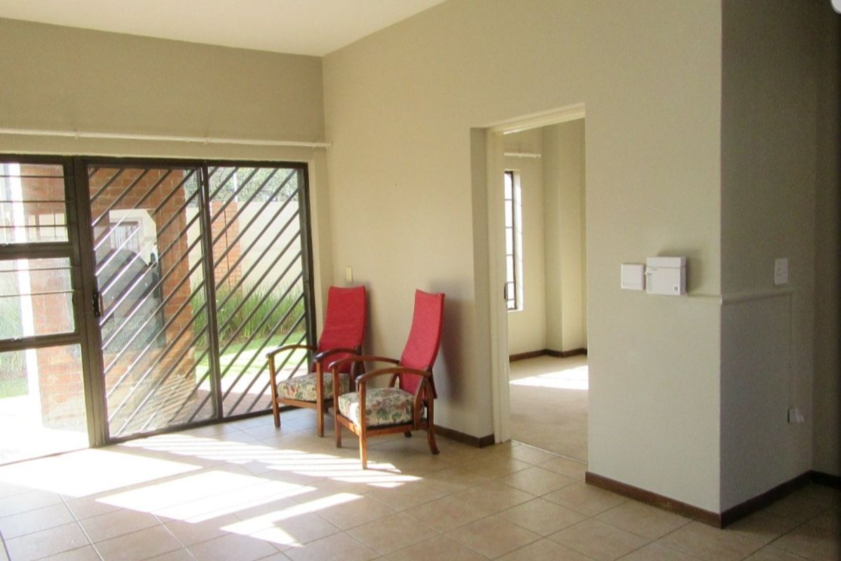 A bright living area featuring neutral tiled flooring and a sliding glass door with security gate, providing access to the exterior.