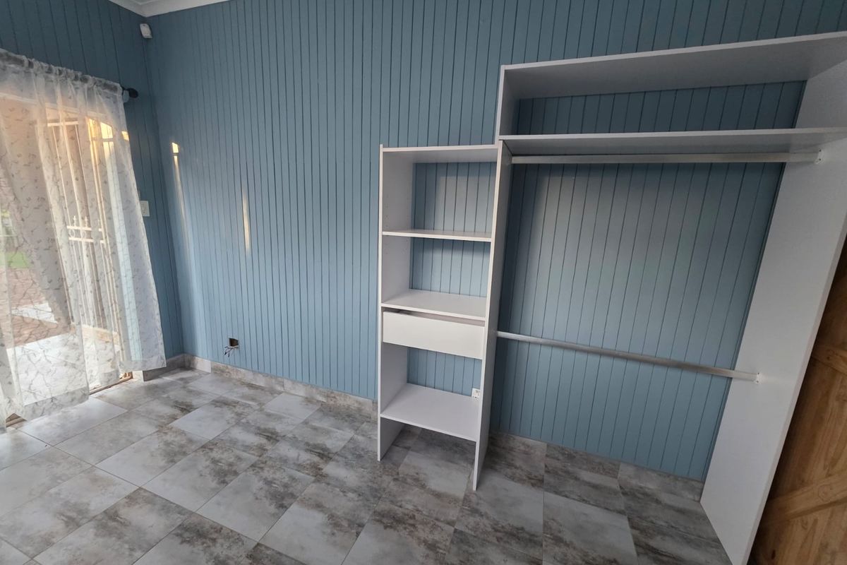 A bedroom featuring blue vertical wall paneling, tiled flooring, and a built-in wardrobe with open shelving and hanging space.