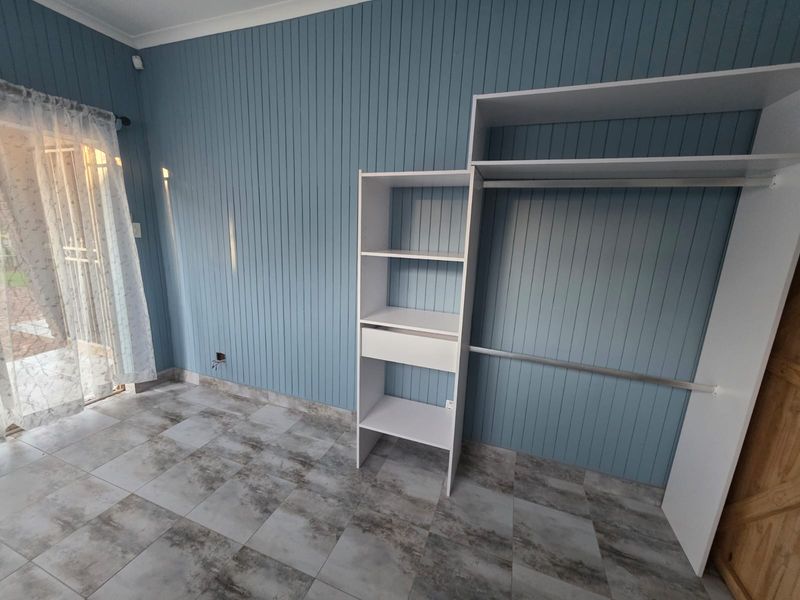 A bedroom featuring blue vertical wall paneling, tiled flooring, and a built-in wardrobe with open shelving and hanging space.