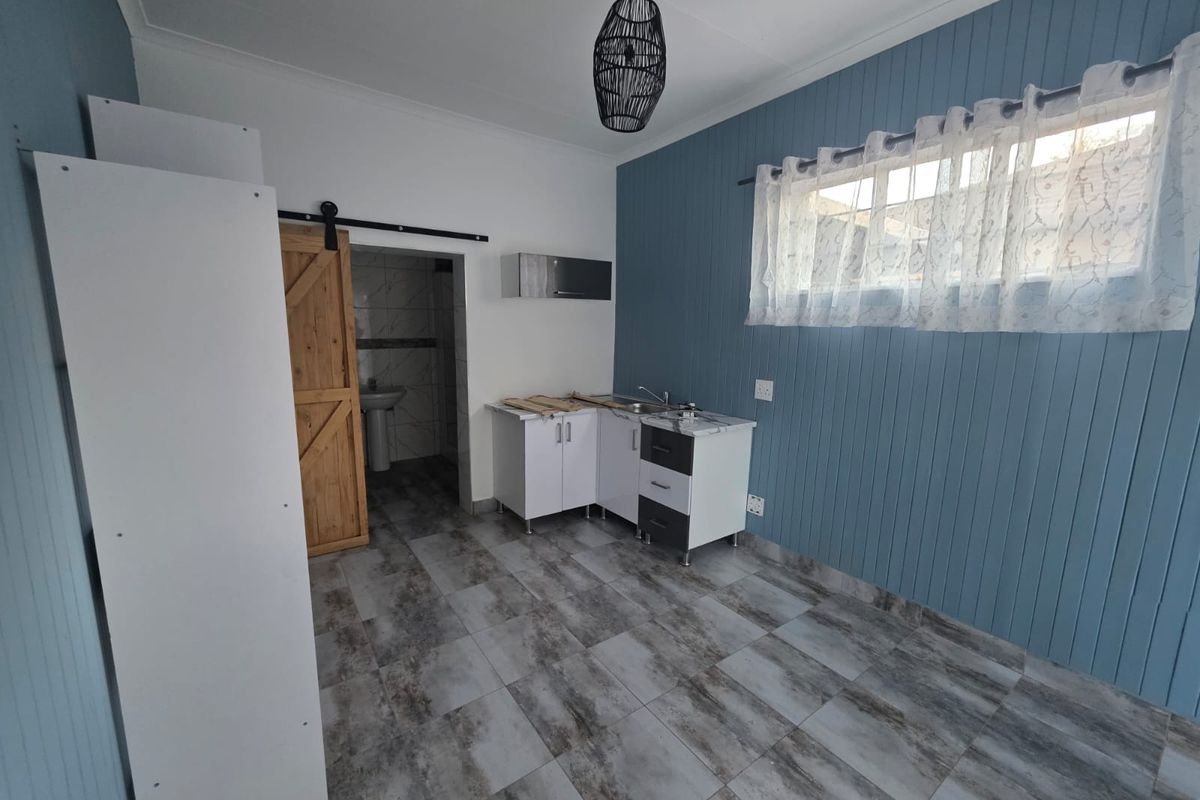 A compact kitchen area featuring modern tiled flooring, blue tongue and groove wall paneling, and a sliding barn door leading to an adjacent bathroom.