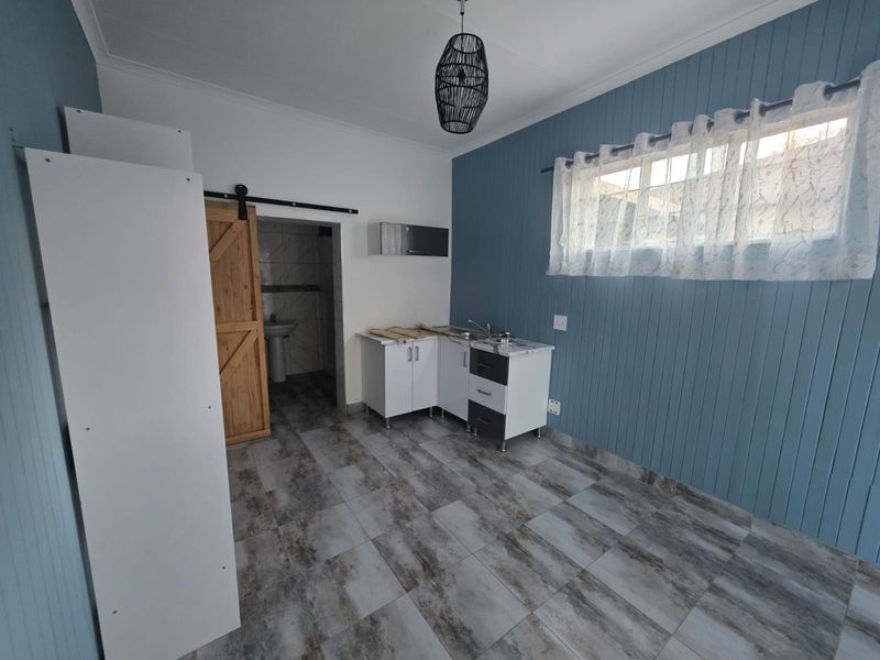 A compact kitchen area featuring modern tiled flooring, blue tongue and groove wall paneling, and a sliding barn door leading to an adjacent bathroom.