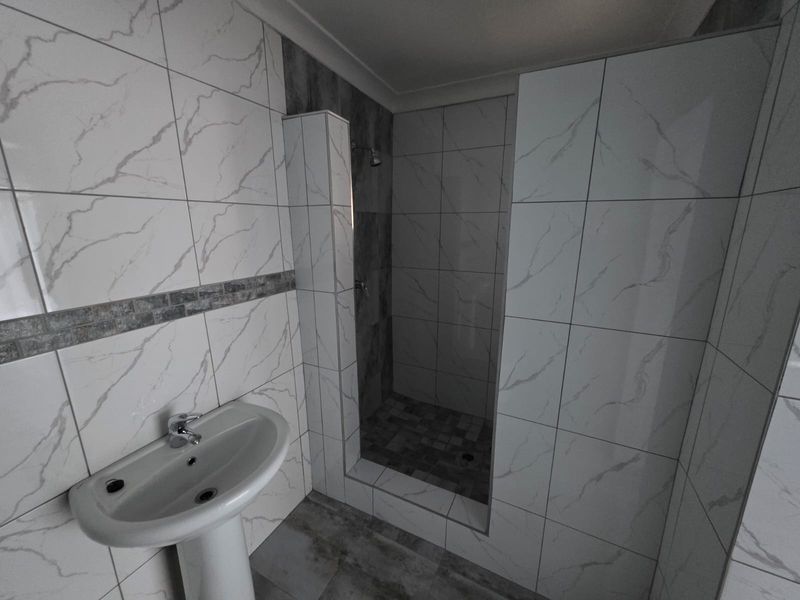 A modern bathroom featuring a pedestal washbasin and a tiled walk-in shower with contemporary marble-effect wall tiles.