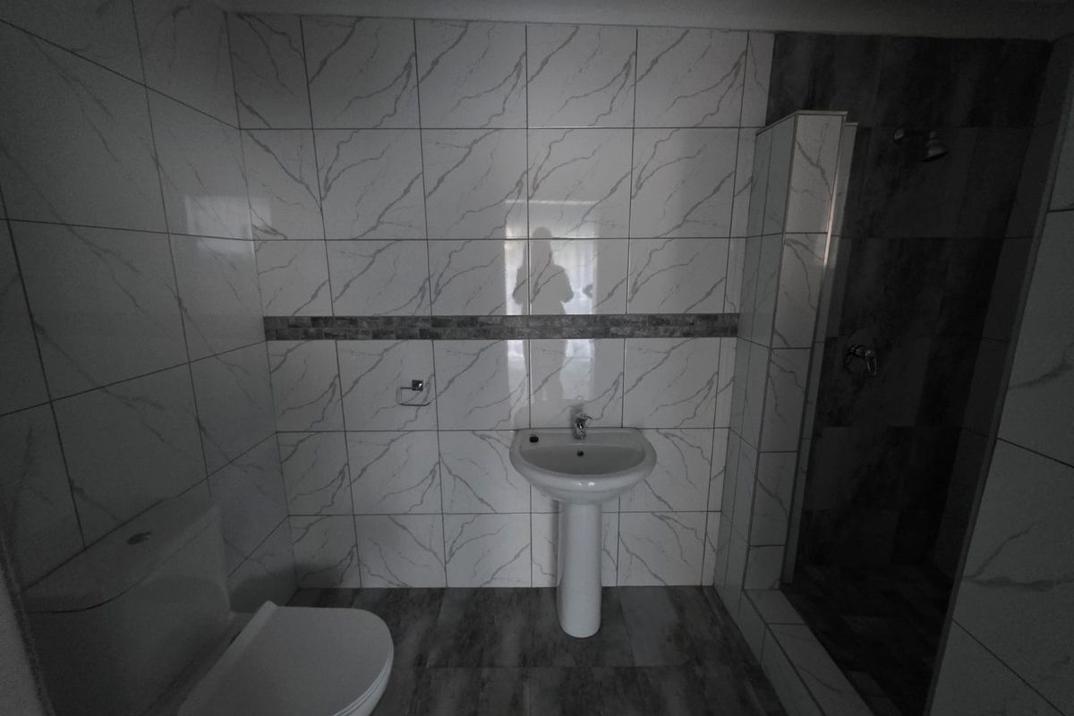 A modern bathroom featuring marble-look wall tiles, a pedestal basin, a toilet, and a separate shower enclosure with dark accent tiling.