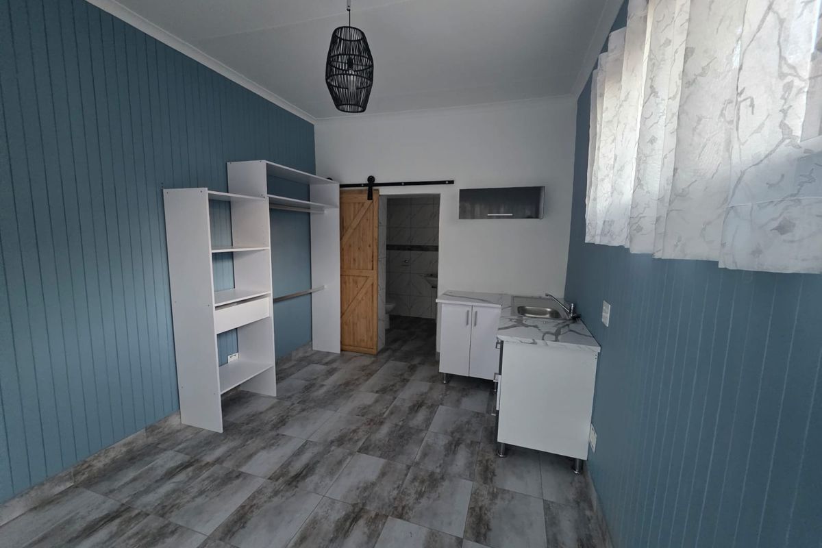 Open-plan studio space featuring blue panelled walls, tiled flooring, a kitchenette area, built-in shelving, and a sliding barn door leading to a bathroom.